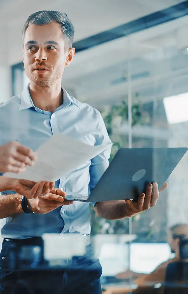 Woman and man holding a paper and computer discussing something in a office
